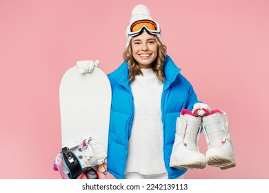 Snowboarder smiling fun woman wears blue suit goggles mask hat ski padded jacket hold snowboard boots isolated on plain pastel pink background. Winter extreme sport hobby weekend trip relax concept
