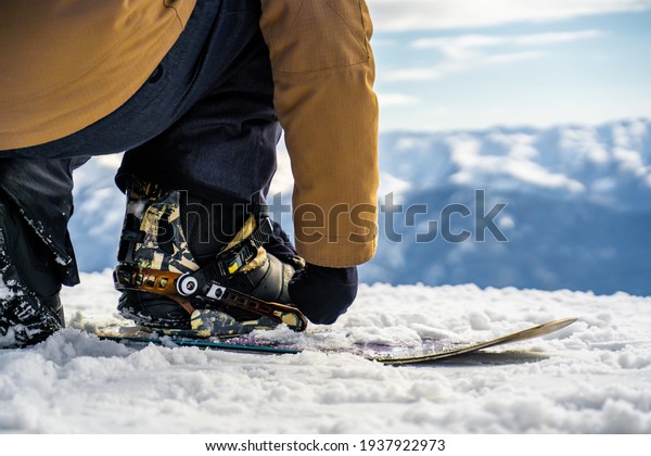 a snowboarder straps on\
a snowboard in close-up . in the background, a view of the\
mountains and snow