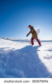 Snowboarder walking through deep fresh snow against blue sky.