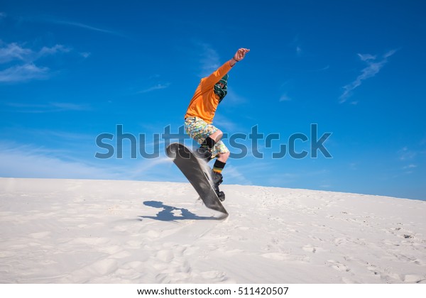 Snowboarder, wearing a scarf to protect against\
sand, is jumping on a sand dune. Sand boarding in desert. Low point\
shooting. Wide\
angle.