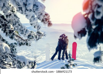 Snowboarders couple man and woman kissing on background of snowy winter mountains and sunset. - Powered by Shutterstock