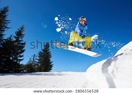 Snowboarding closeup in jump on blue sky background. Portrait of young man snowboarding in winter. Ski season and winter sports concept