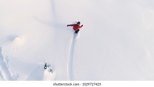 Snowboarding Overhead Top Down View Of Snowboarder Riding Through Fresh Powder Snow Down Ski Resort Or Backcountry Slope - WInter Extreme Sports Background