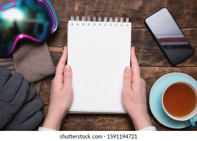 Snowboarding Tips Mock Up. Snowboard Gear List Template. Blank Page Notepad With Copy Space And Snowboard Googles, Cuf Of Black Tea, Mobile Phone On Brown Wooden Table Flat Lay Background.