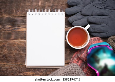 Snowboarding Tips Mock Up. Snowboard Gear List Template. Blank Page Notepad With Copy Space And Snowboard Googles, Cuf Of Black Tea On Brown Wooden Table Flat Lay Background.