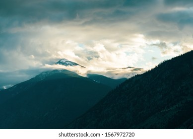 Snowcapped mountain peak surrounded by dramatic clouds and mist with sunlight
