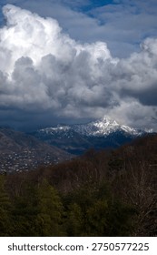 Snow-capped mountain peaks under dramatic white storm clouds and blue sky