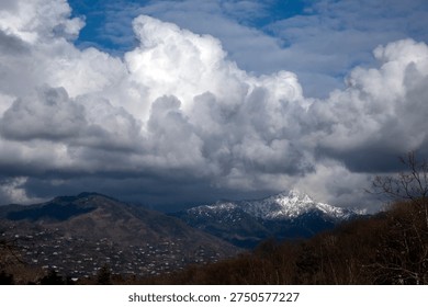 Snow-capped mountain peaks under dramatic white storm clouds and blue sky