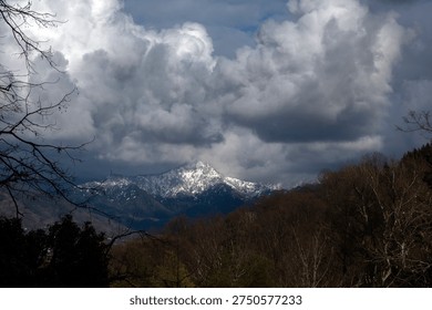 Snow-capped mountain peaks under dramatic white storm clouds and blue sky