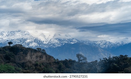 Snow-Capped Mountain Range Beneath Dramatic Clouds and Forested Hills
