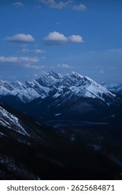 Snow-capped mountain range under a deep blue sky with scattered clouds, capturing the stillness of twilight in a rugged landscape.
