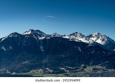 The snow  capped mountains between Brand   Feldkirch still bear their snow fields in spring   rise up into the cloudless blue sky  Only an airplane draws white  arched track in the deep blue