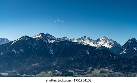 The snow  capped mountains between Brand   Feldkirch still bear their snow fields in spring   rise up into the cloudless blue sky  Only an airplane draws white  arched track in the deep blue