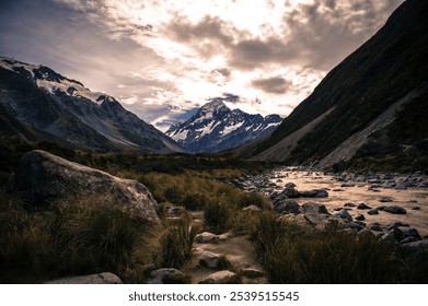 Snowcapped mountains, rocky stream, grassy valley, dramatic clouds, serene landscape. - Powered by Shutterstock