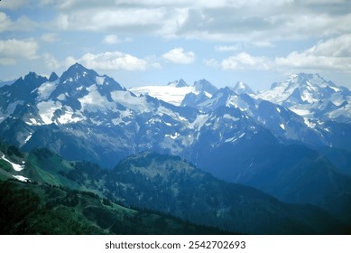 Snow-capped mountains tower above clouds, casting shadows over lush valley with evergreen forests, creating stunning contrast. Breathtaking scenery captures essence of wilderness and tranquility - Powered by Shutterstock