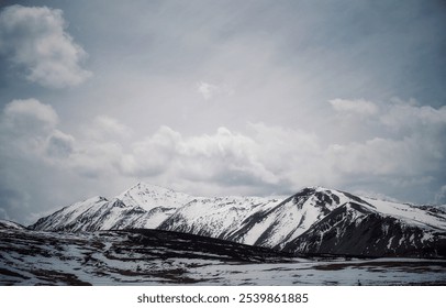 Snow-capped mountains under a cloudy sky with rugged terrain in the foreground - Powered by Shutterstock