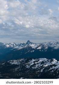 Snow-covered alpine mountains and dramatic cloudy sky over rugged wilderness in British Columbia, Canada.