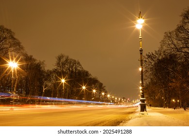 a snow-covered avenue with burning lanterns on a winter evening. along the road there are black trees against the sky