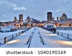 Snow-covered benches, pier, waterfront walkway, harbor, and downtown Montreal after sunset in winter - Montreal, Canada