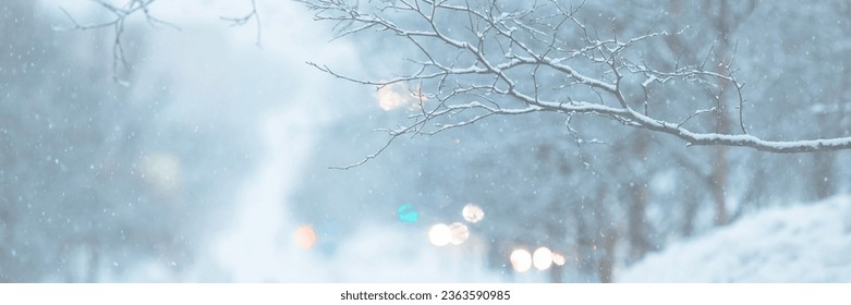 Snow-covered branches and snowflakes in the air. Glittering lights out of focus. Cold winter snowy weather. Evening twilight. Shallow depth of field and blurry background. Wide panoramic background.