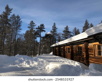 Snow-covered cabin in a forest with clear blue sky. - Powered by Shutterstock