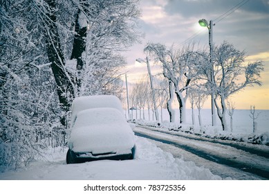 Snow-covered car parked next to road with street lights. Winter snow calamity. Countryside road in winter. - Powered by Shutterstock