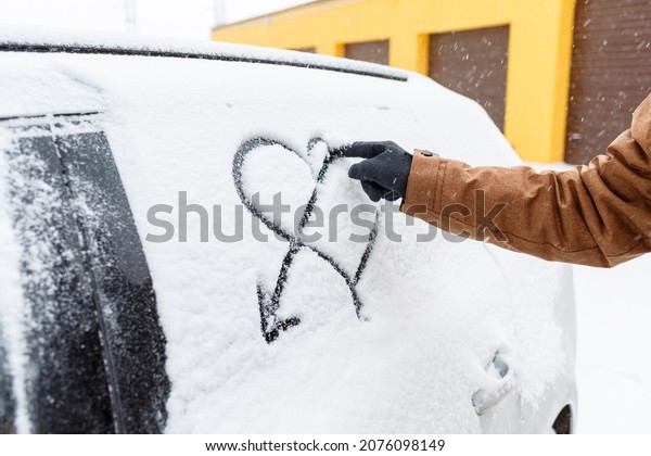 A snow-covered car stands on the street in winter.\
Snow on the windows of cars. Painted heart in the snow on the car\
window