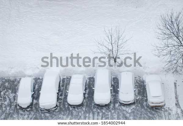 Snow-covered cars during snowfall in the city in\
the parking lot after snowfall top\
view