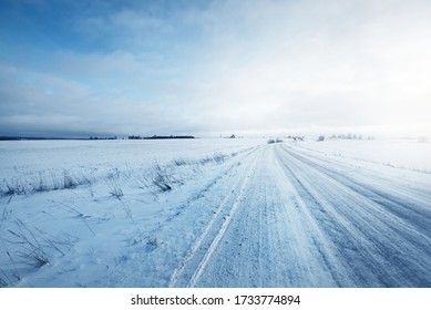 Snow-covered Country Road Through The Fields After A Blizzard At Sunset. Old Rustic House In The Background. Winter Rural Scene. Dramatic Sky, Colorful Cloudscape. Ice Desert. Lapland, Finland