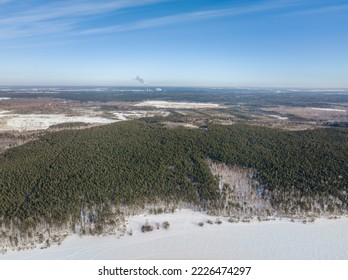 Snow-covered forest on lake shore with ice at sunset and the city on horizon, auerial view. Beautiful winter forest landscape. Lake Shartash and Yekaterinburg, Russia