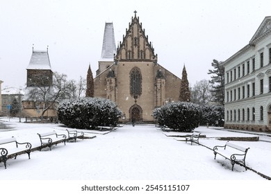 Snow-covered landscape featuring a historic church and benches in a quiet European town during winter - Powered by Shutterstock