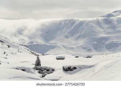 Snow-covered mountain with dramatic clouds spilling over the ridge under overcast sky, alpine winter landscape.