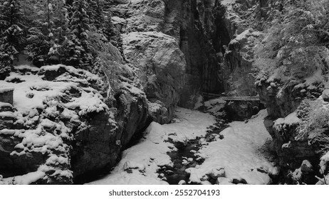 Snow-covered mountain gorge with narrow icy stream, evergreen trees and overcast winter sky, showcasing the beauty of snow-clad rocks and trees along a cold, snowy gorge - Powered by Shutterstock