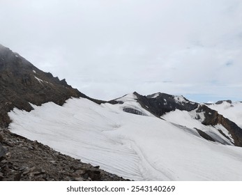 A snow-covered mountain peak, glistening under bright sunlight, with soft, powdery snow blanketing the rugged terrain. Crisp, clear skies frame the summit, and distant mountain ranges add depth to the - Powered by Shutterstock