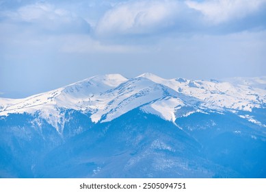 Snow-covered mountain peak under clear blue sky, with patches of snow on slopes and scattered trees. Serene winter landscape contrasts sharply with the dark, forested areas below. Blyznytsya, Ukraine - Powered by Shutterstock