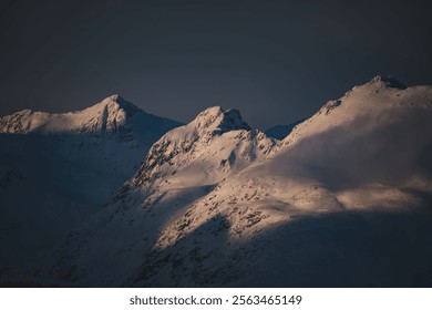 Snow-covered mountain peaks bathed in warm light at dusk, creating a serene and dramatic landscape. - Powered by Shutterstock