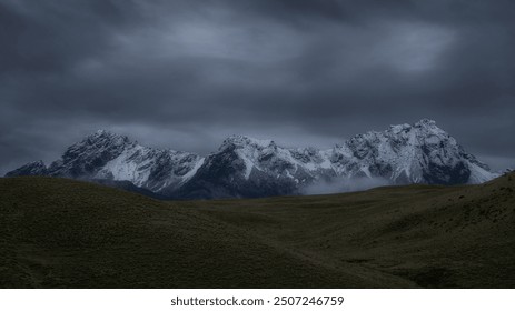 Snow-covered mountain peaks under a dramatic, cloudy sky, showcasing nature’s raw, moody beauty - Powered by Shutterstock