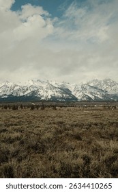 Snow-covered mountain range beneath a dramatic sky with sagebrush plains stretching out in the foreground.