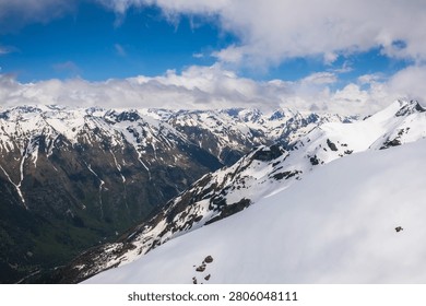 Snow-covered mountain range features rugged peaks and valleys under a blue sky with scattered clouds, creating a stunning natural landscape