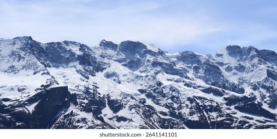 Snow-covered mountain range features towering peaks and steep cliffs under a bright blue sky, offering a stunning view of nature's beauty and adventure opportunities