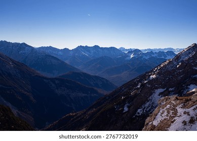 Snow-covered mountain range with sharp peaks and deep valleys under a bright blue sky, highlighting the natural beauty of a remote alpine region