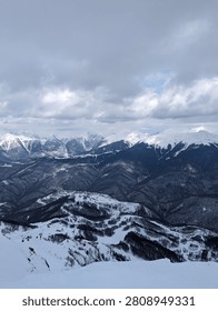 Snow-covered mountain range under a cloudy sky, showcasing a breathtaking winter landscape.