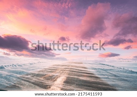 Snow-covered Open Slippy Road During A Snowstorm Blizzard In Winter. Altered Colorful Sunset Sunrise Sky. Dangerous Motion. Strong Wind In Winter Sunny Day. Dangerous Weather Conditions Blizzard In