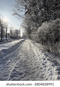 Snow-covered road bordered by trees during a clear winter afternoon. The image conveys the concept of quiet travel, seasonal landscape, and cold weather conditions.