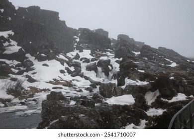 Snow-covered rocky landscape with a small waterfall under overcast sky. - Powered by Shutterstock