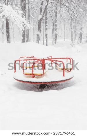 Snow-covered round carousel for children on the playground in winter. Equipment for children.