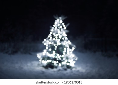Snow-covered spruce tree illuminated by the garland of white lights blurred in bokeh, close-up. Dark twilight evergreen forest in the background. Winter landscape. Christmas celebration, decoration - Powered by Shutterstock