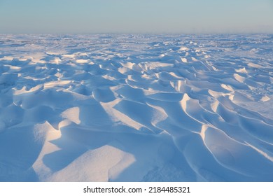 Snow-covered tundra. Winter arctic landscape.  Cold frosty weather. On the surface of the snow, there are sastrugi (patterns formed by erosion of snow by wind). The harsh climate of the polar region.
