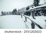 Snow-covered wooden fence stretching into the snowy wilderness, creating a rustic and serene winter scene. The untouched snow and evergreen trees evoke peace and natural beauty