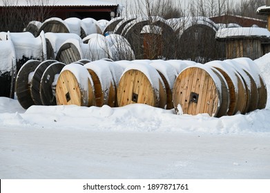 Snow-covered wooden spools with electric cable. Different size coils outdoors. 
Electrical cable plant